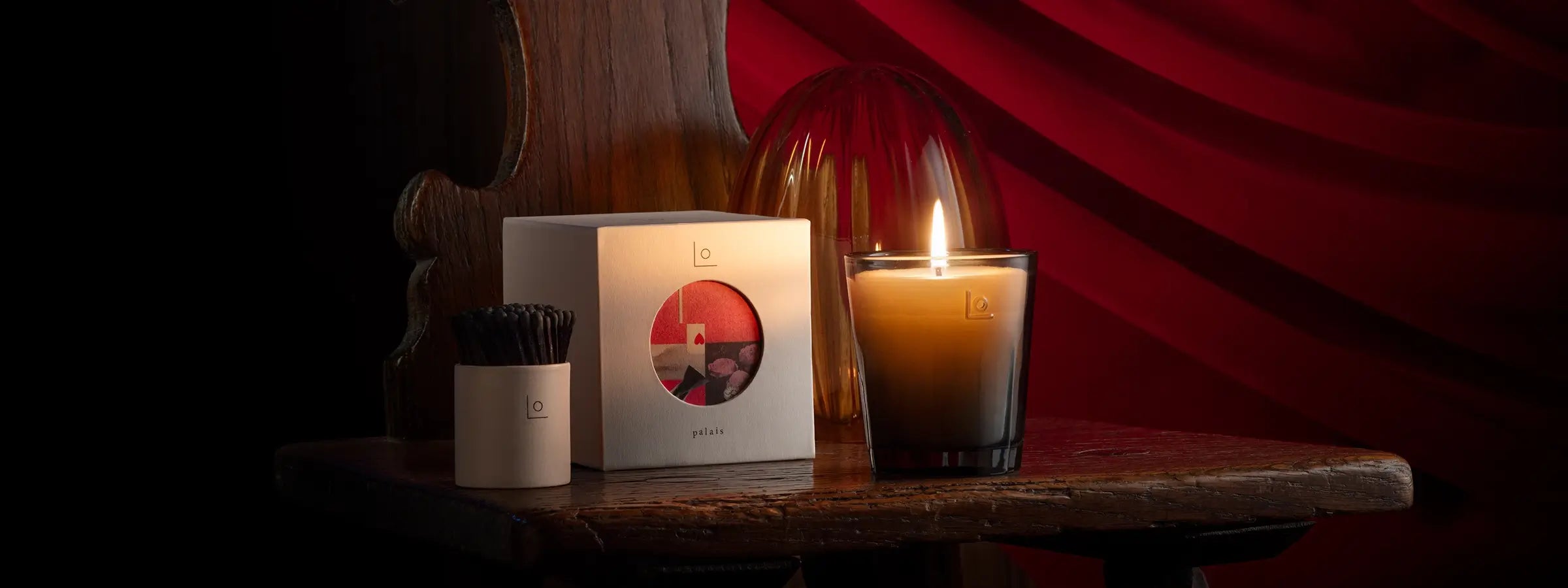 Romantic scene with red background showcasing lit Palais Scented Candle glass cloche and stoneware match pot